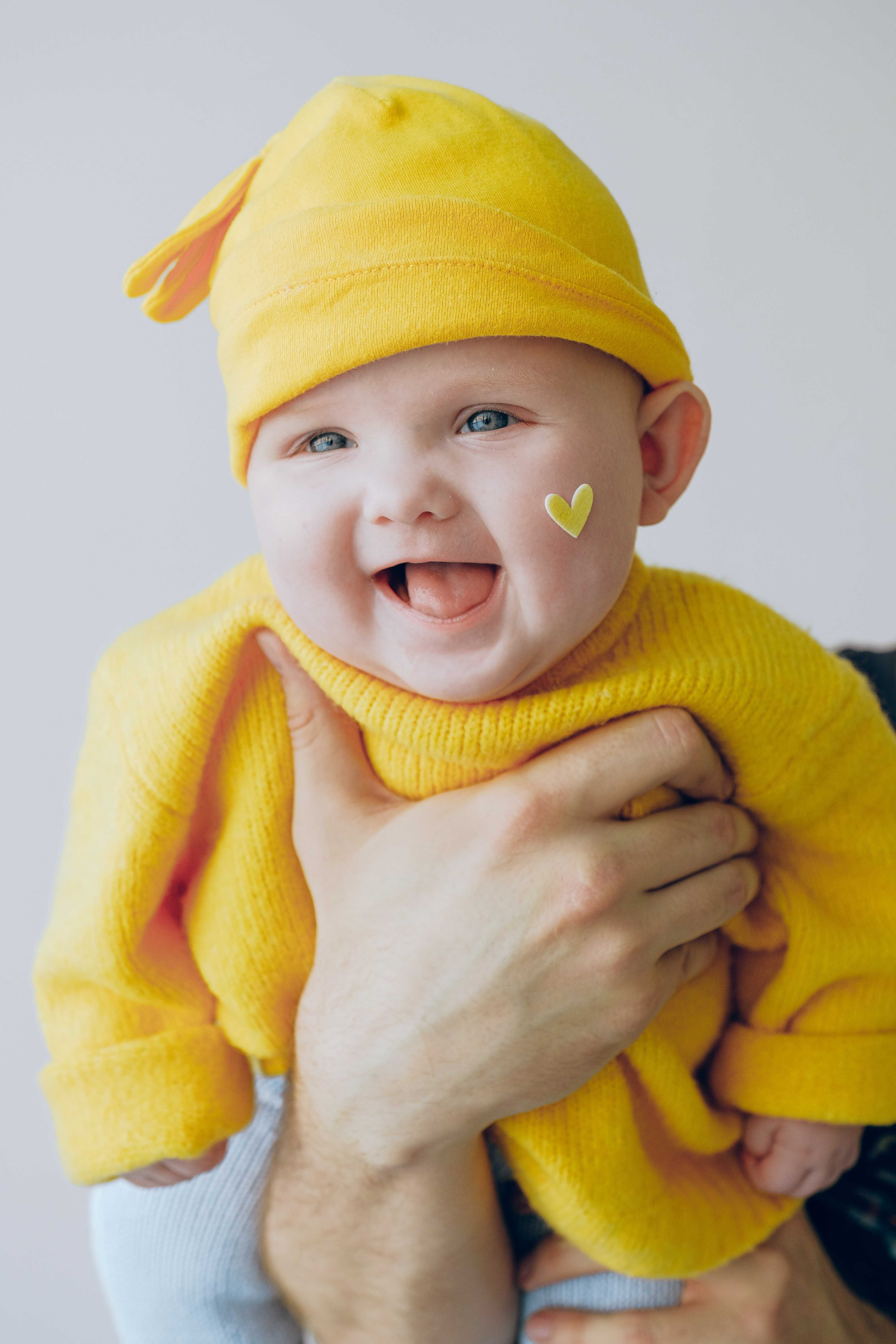 Un bambino vestito di giallo, tenuto in braccio dal papà, che sorride.